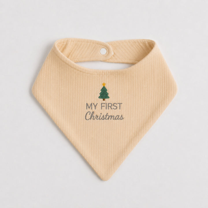 Cream baby bib embroidered with a green Christmas tree topped with a gold star and the words “My First Christmas” in grey, photographed on a clean white background.