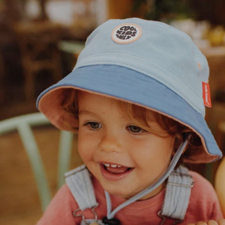 Smiling toddler wearing a light blue and royal blue Hello Hossy bucket hat with chin strap.