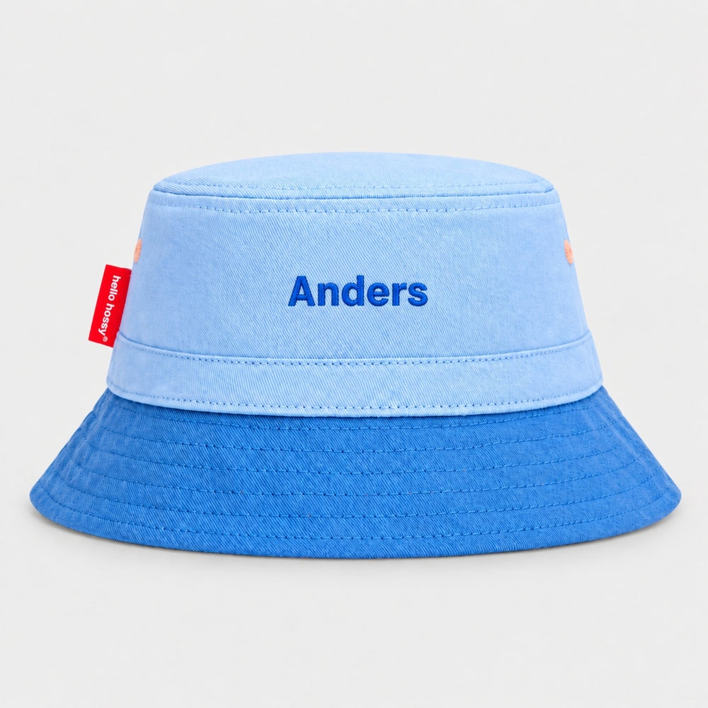 Back view of a blue Hello Hossy bucket hat personalised with “Anders” in royal blue block embroidery and red side tag.