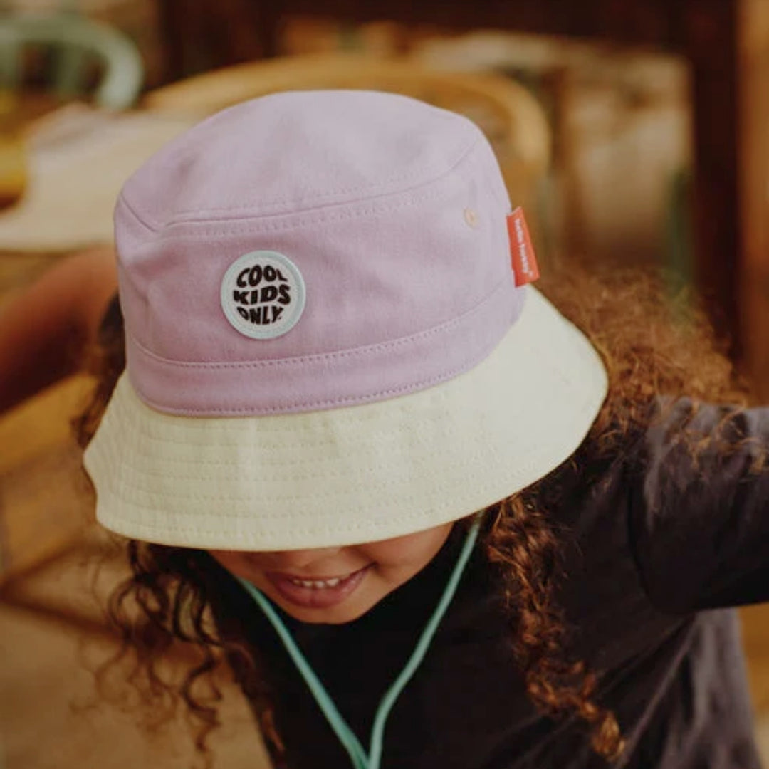 Young child wearing a lilac and cream Hello Hossy bucket hat with “Cool Kids Only” patch and mint chin strap.