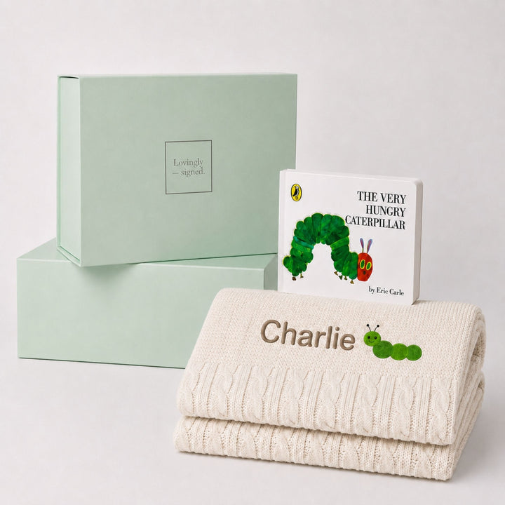 Personalised cream cable knit baby blanket embroidered with the name Charlie and a caterpillar motif, paired with The Very Hungry Caterpillar and a Lovingly Signed gift box.