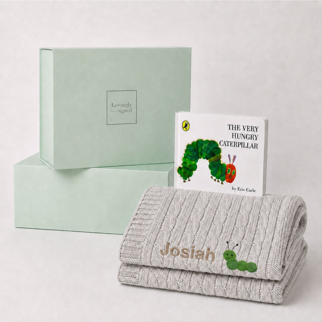 Personalised grey cable knit baby blanket embroidered with the name Josiah and a caterpillar motif, paired with The Very Hungry Caterpillar and a Lovingly Signed gift box.