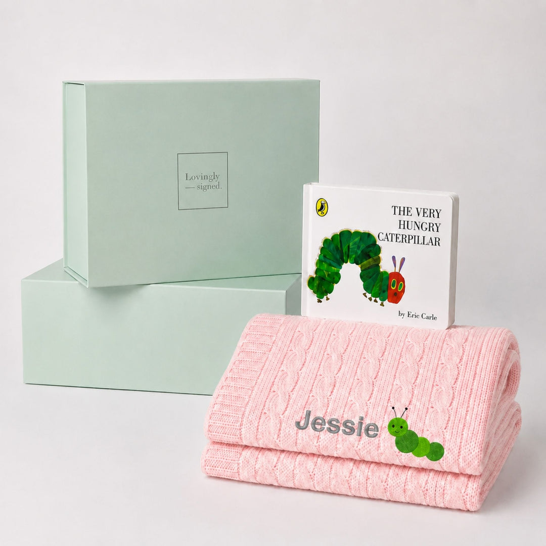 Personalised pink cable knit baby blanket embroidered with the name Jessie and a caterpillar motif, paired with The Very Hungry Caterpillar and a Lovingly Signed gift box.