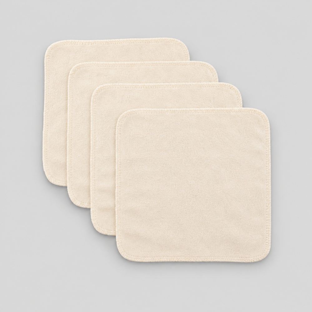 Four cream organic cotton baby face cloths arranged in an overlapping stack on a light grey studio background.