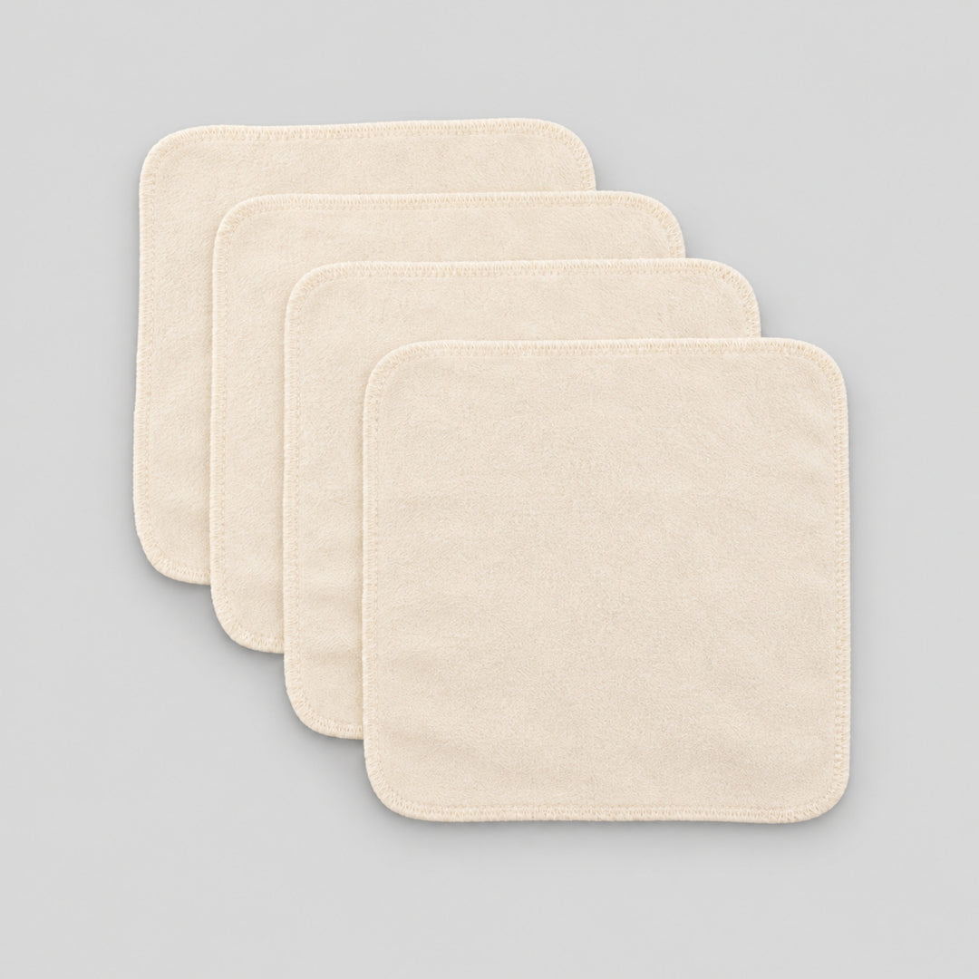 Four cream organic cotton baby face cloths arranged in an overlapping stack on a light grey studio background.