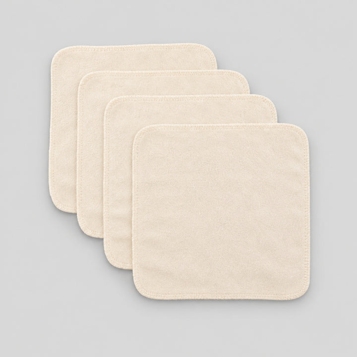 Four cream organic cotton baby face cloths arranged in an overlapping stack on a light grey studio background.