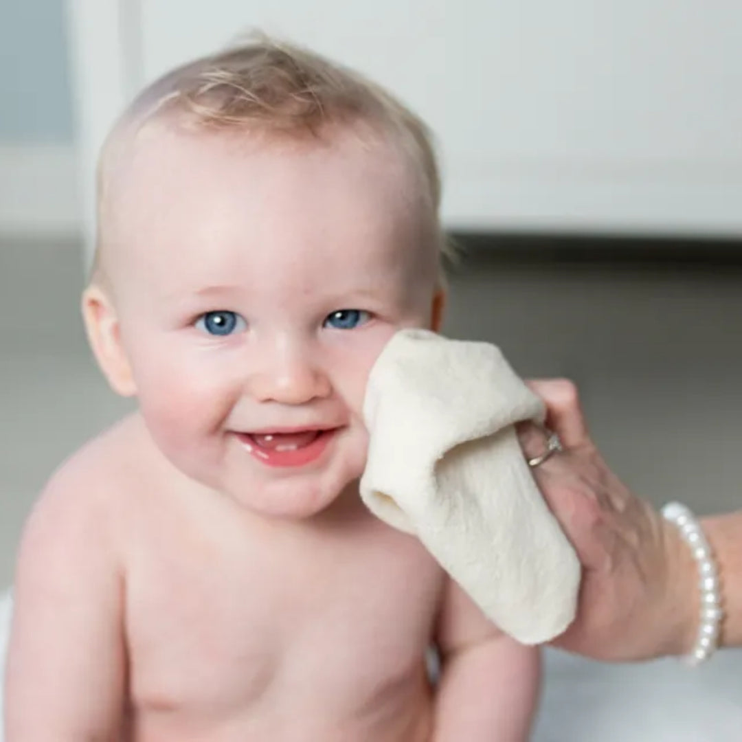 Smiling baby having their face gently wiped with a soft cream organic cotton washcloth.