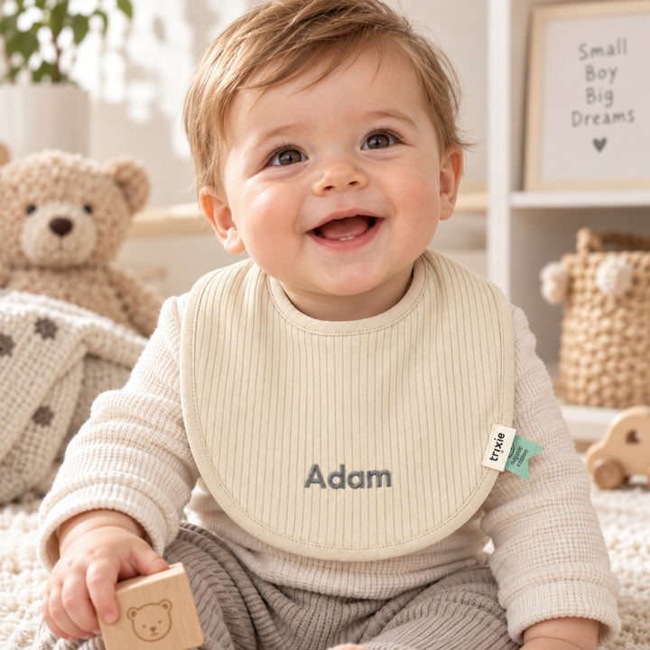 Baby boy wearing personalised beige Trixie baby bib with Adam embroidered, UAE