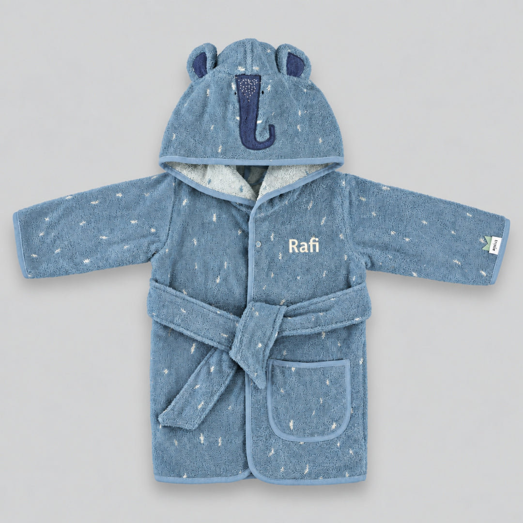 Front view of a dusty blue children’s elephant bathrobe laid flat on a seamless light grey studio background. The robe features an elephant-face hood with rounded ears and a navy embroidered trunk, white speckled detailing, matching belt and front pocket, personalised with the name “Rafi” in cream embroidery on the chest.