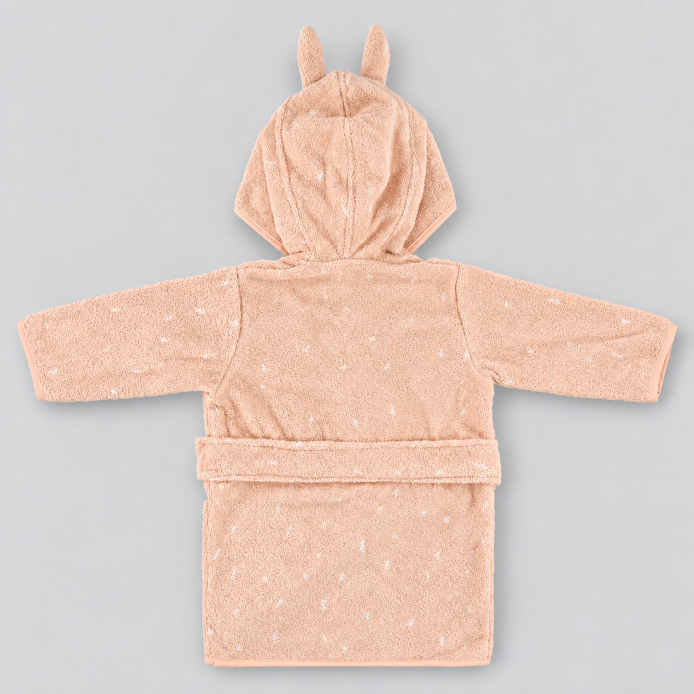 Back view of a soft blush-pink children’s rabbit bathrobe laid flat on a seamless light grey studio background. The robe features a hood with long upright bunny ears, subtle white speckled detailing, long sleeves, and a matching waist belt.