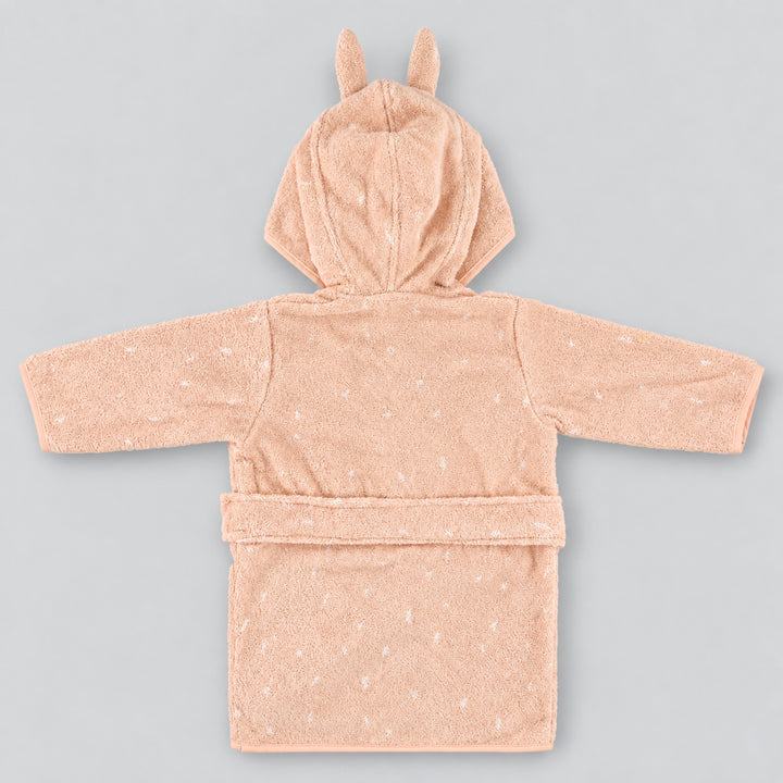 Back view of a soft blush-pink children’s rabbit bathrobe laid flat on a seamless light grey studio background. The robe features a hood with long upright bunny ears, subtle white speckled detailing, long sleeves, and a matching waist belt.