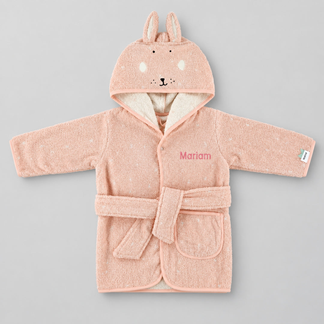 Front view of a blush-pink children’s rabbit bathrobe laid flat on a seamless light grey studio background. The hood features long bunny ears and an embroidered rabbit face, with a cream inner lining, matching belt and front pocket. The robe is personalised with the name “Mariam” in pink embroidery on the chest.