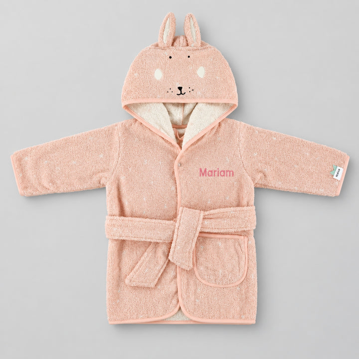 Front view of a blush-pink children’s rabbit bathrobe laid flat on a seamless light grey studio background. The hood features long bunny ears and an embroidered rabbit face, with a cream inner lining, matching belt and front pocket. The robe is personalised with the name “Mariam” in pink embroidery on the chest.