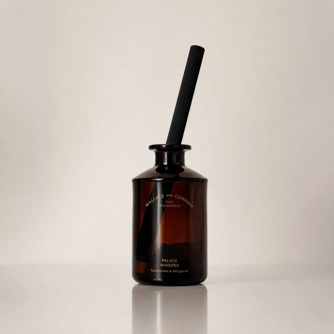 Wallace and Company “Palace Whisper – Cardamom & Bergamot” reed diffuser in a dark amber glass bottle with a single black diffuser stick, photographed against a warm neutral studio background.