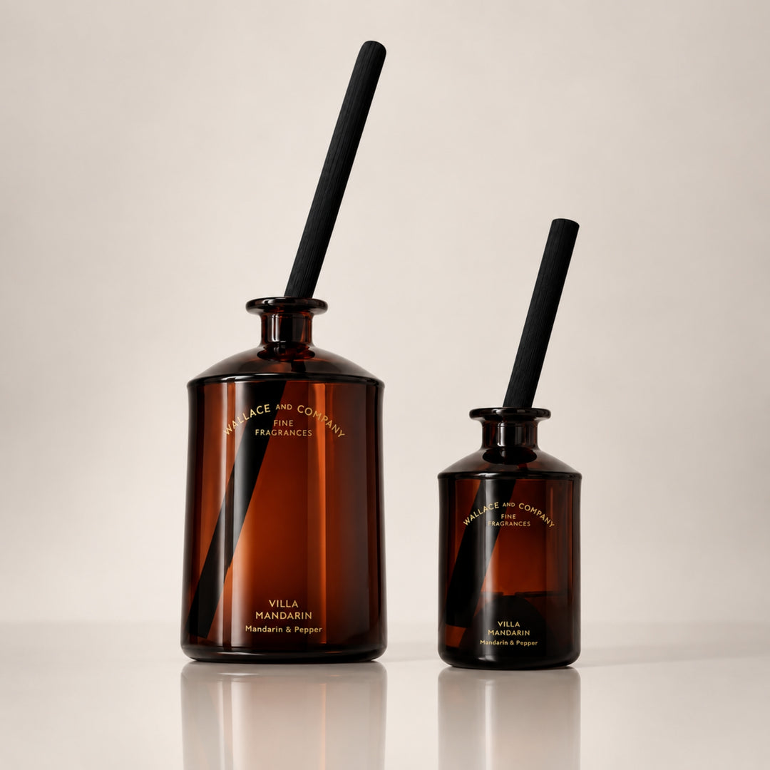 Large and small Wallace and Company “Villa Mandarin – Mandarin & Pepper” reed diffusers in dark amber glass bottles with black diffuser sticks, displayed side by side against a warm neutral studio background.
