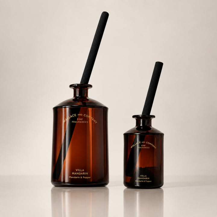 Large and small Wallace and Company “Villa Mandarin – Mandarin & Pepper” reed diffusers in dark amber glass bottles with black diffuser sticks, displayed side by side against a warm neutral studio background.