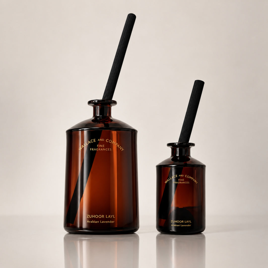 Large and small Wallace and Company “Zuhoor Layl – Arabian Lavender” reed diffusers in dark amber glass bottles with black diffuser sticks, displayed side by side against a warm neutral studio background.
