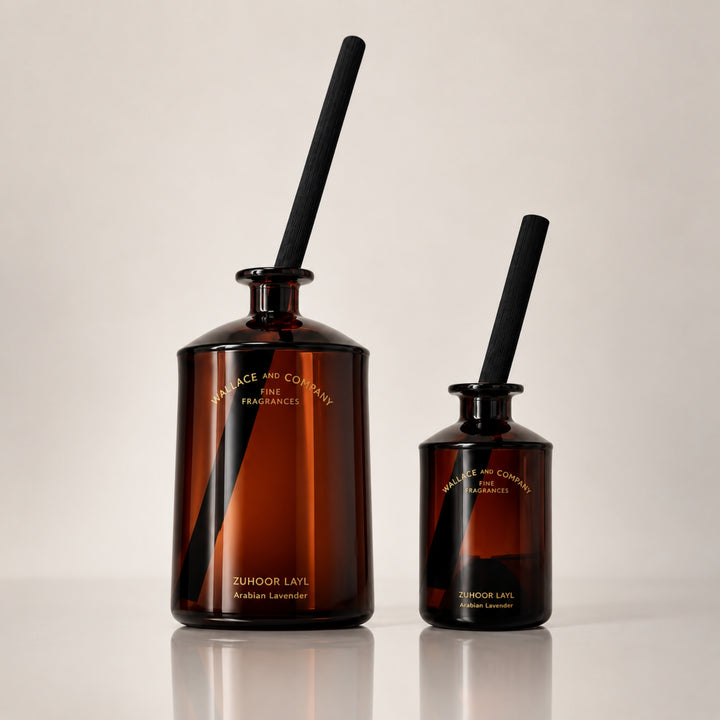 Large and small Wallace and Company “Zuhoor Layl – Arabian Lavender” reed diffusers in dark amber glass bottles with black diffuser sticks, displayed side by side against a warm neutral studio background.